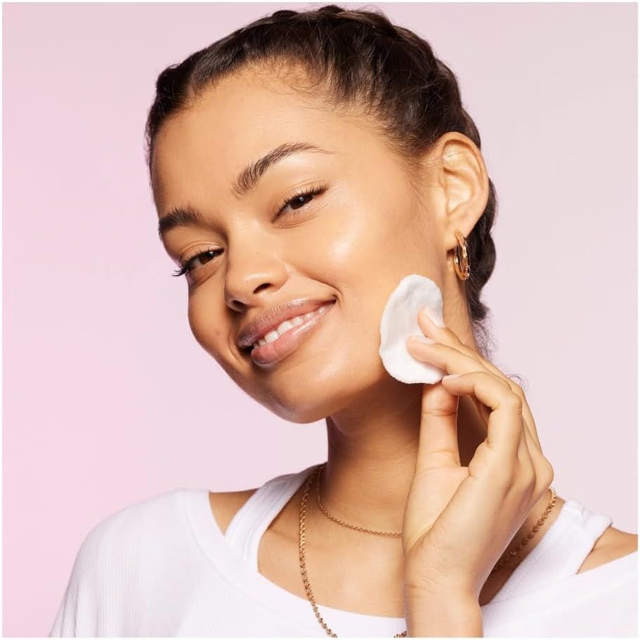 Frau verwendet Wattepad auf Gesicht. Sie lächelt. Hintergrund rosa.