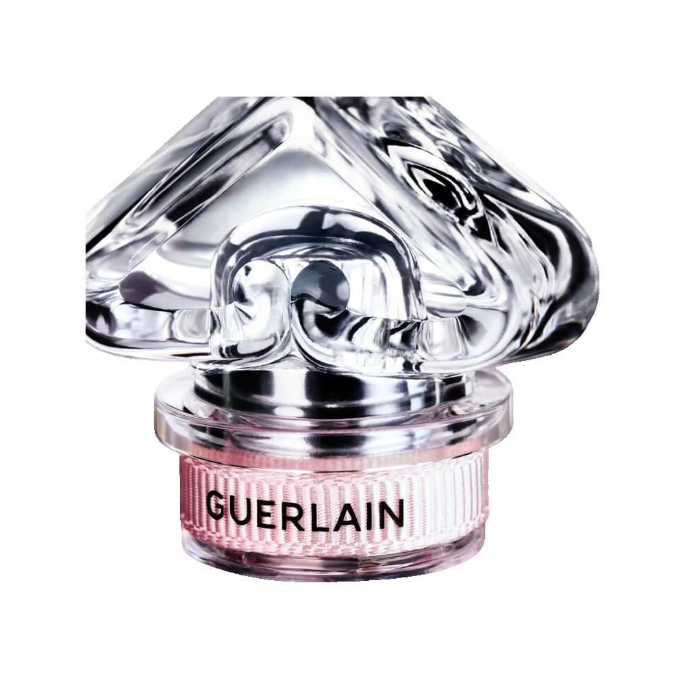 Nahaufnahme einer Parfümflasche mit einem transparenten, blütenförmigen Deckel. Der Name GUERLAIN ist auf dem Flakon zu sehen.