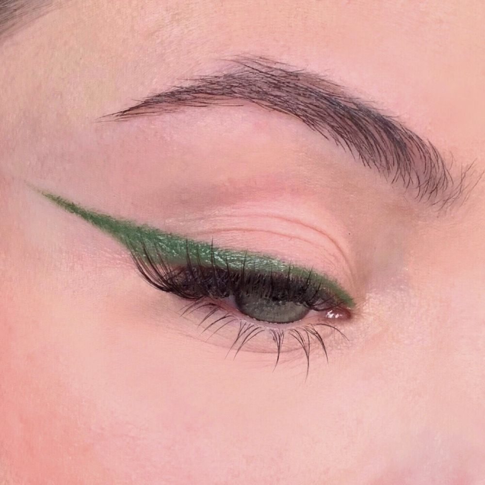 Grüner Eyeliner auf einem Auge. Präzise Linie entlang des oberen Wimpernkranzes. Augenbraue sichtbar.