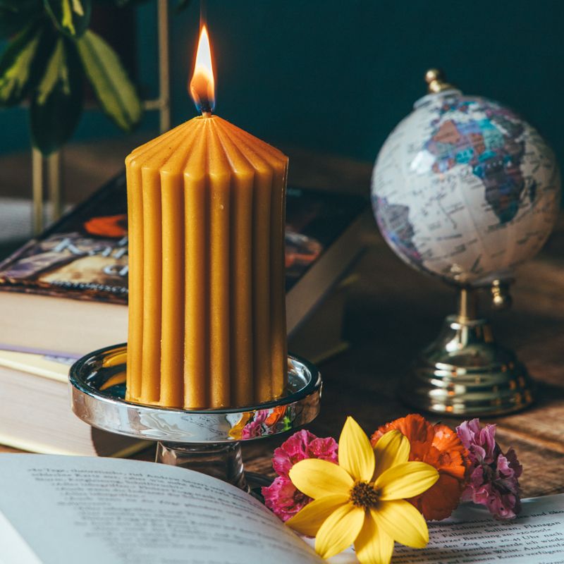 Brennende gelbe Wachskerze auf silbernem Kerzenhalter. Auf einem Tisch mit Buch, Globus und Blumen dekoriert.