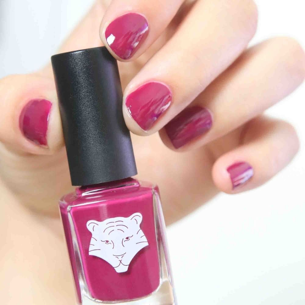 Nagellackflasche und lackierte Nägel. Pinkfarbener Nagellack und lackierte Nägel. Flasche mit Tigerlogo.