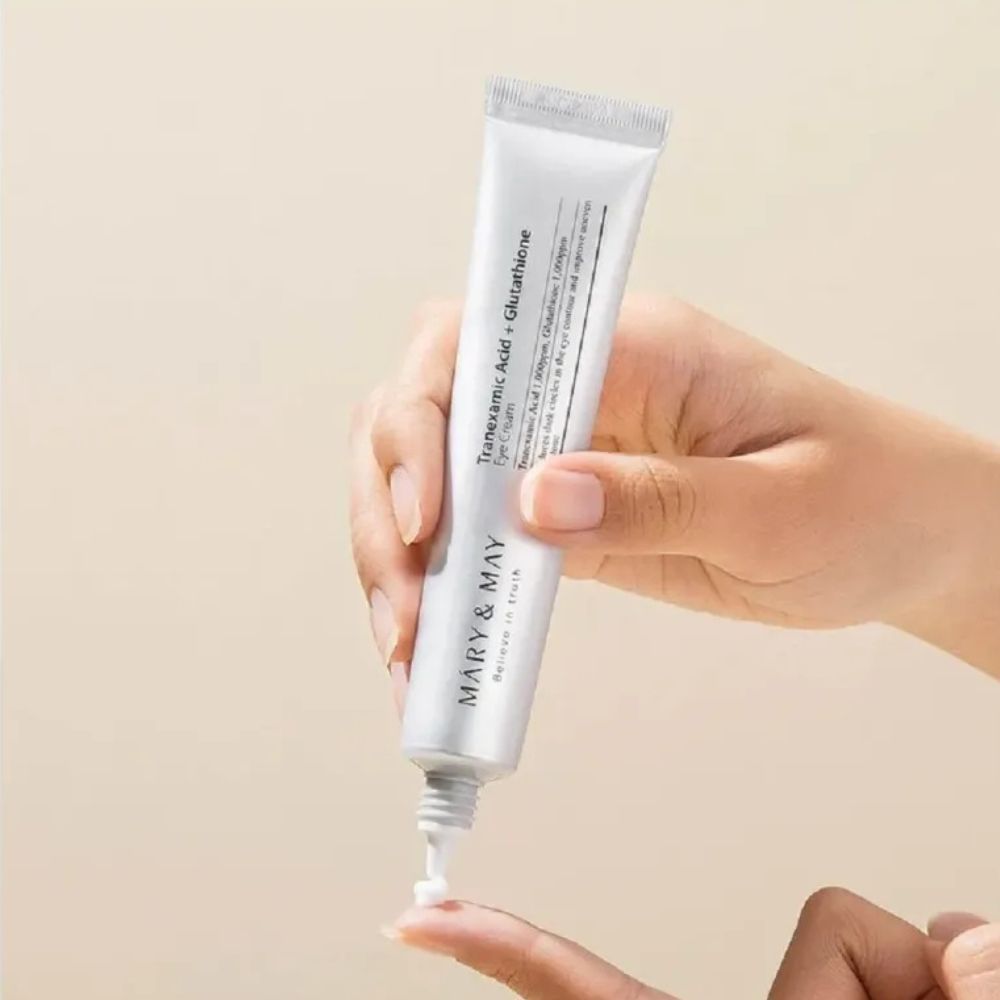 Hand hält eine Tube Mary & May Augencreme, eine kleine Menge wird auf einen Finger aufgetragen.