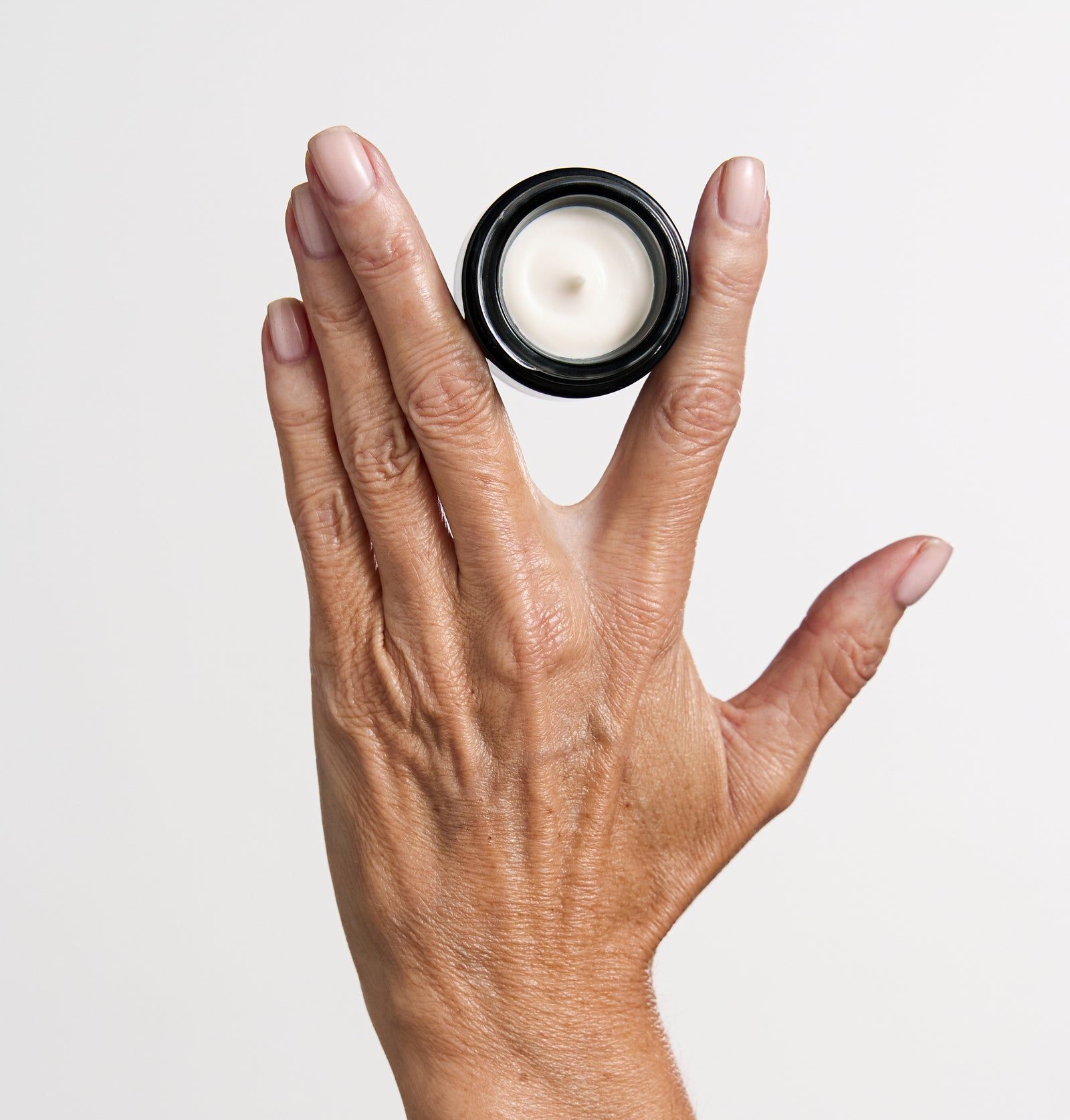 Hand hält einen schwarzen Tiegel mit weißer Creme. Schwarzer Deckel, weißer Inhalt. Helle Haut.