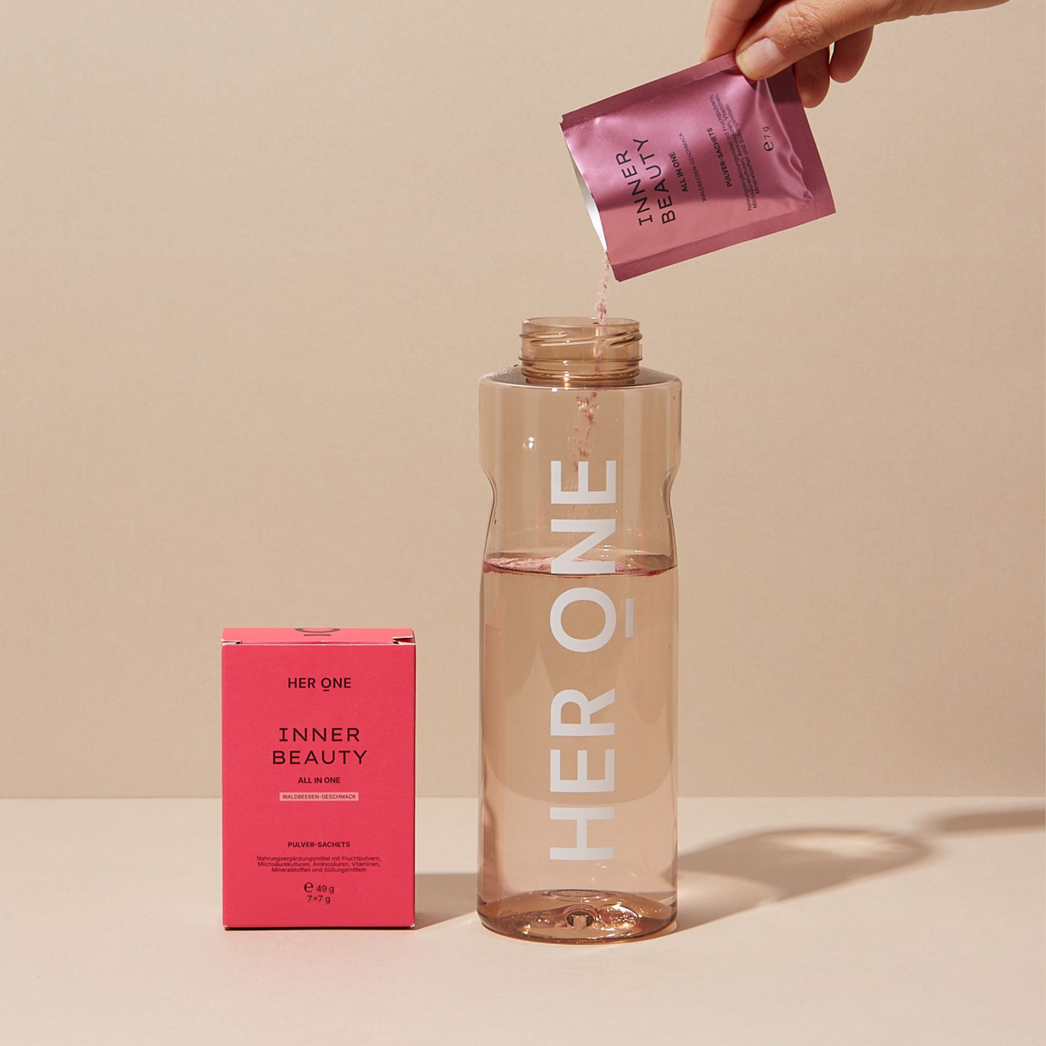 Hand gießt Pulver aus einem Sachet in eine Flasche. Flasche und Produktverpackung sind sichtbar.