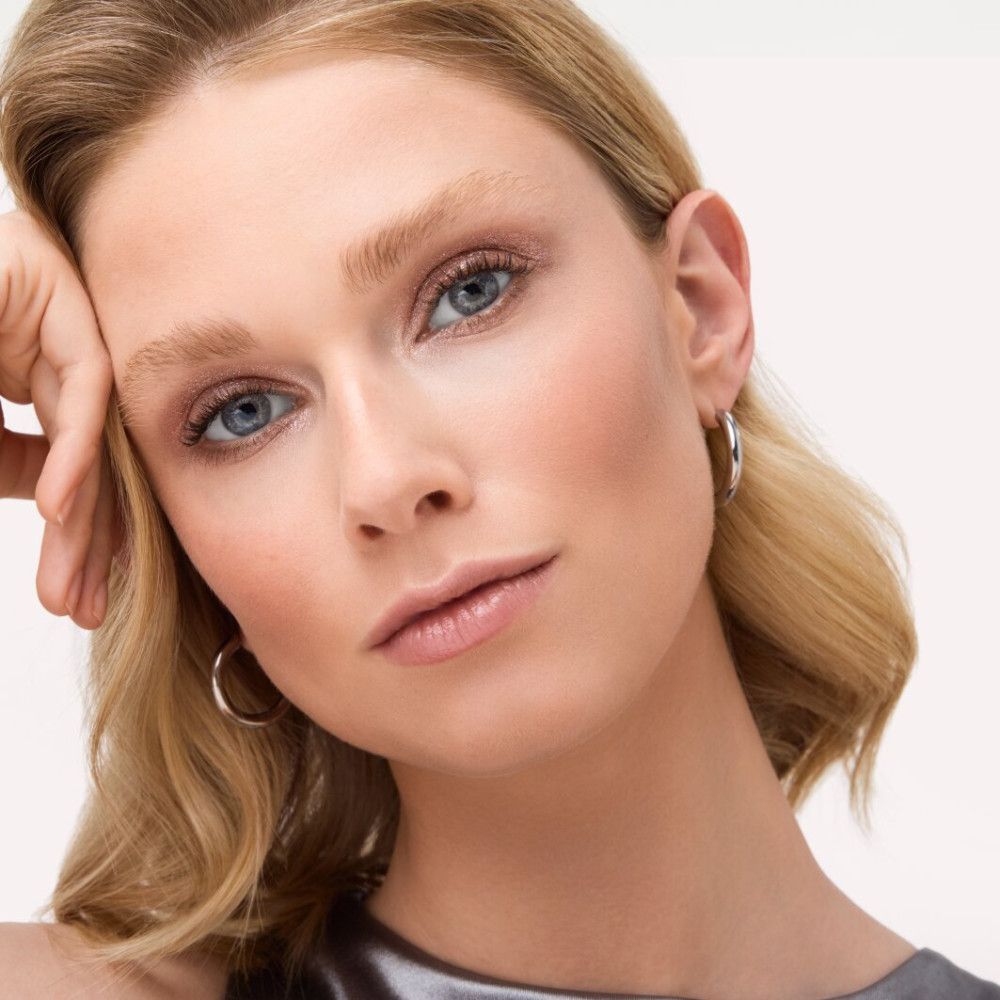 Porträt einer Frau mit blonden Haaren und blauem Augen-Make-up. Sie stützt den Kopf auf die Hand.