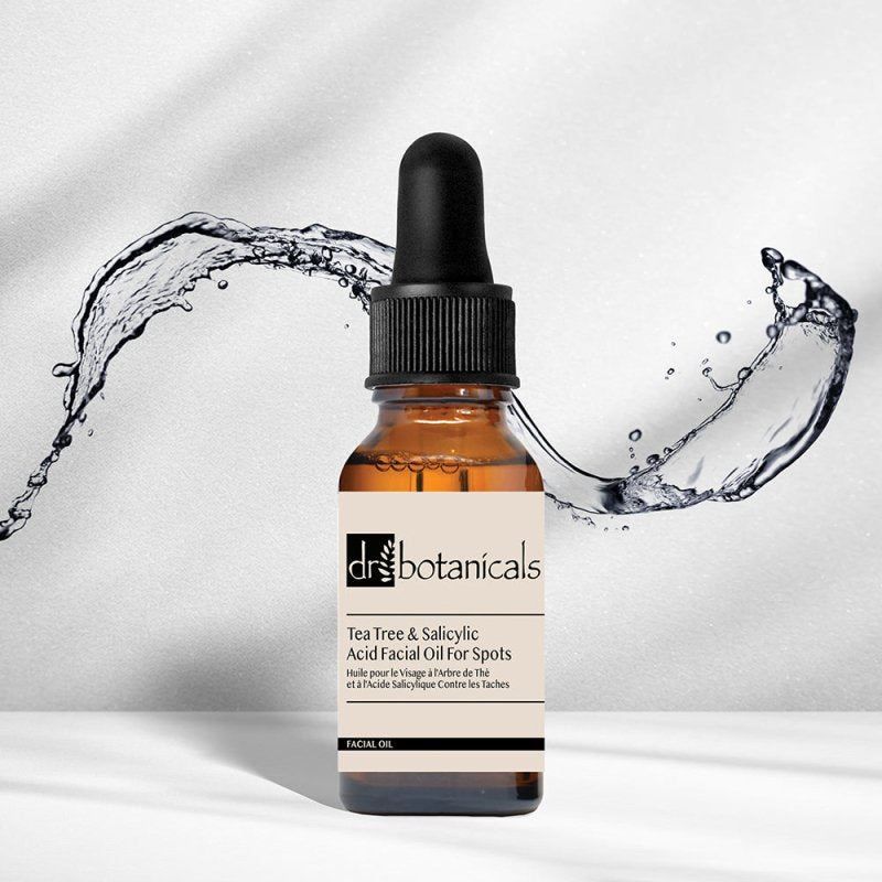 Dr. Botanicals Gesichtsöl mit Teebaumöl und Salicylsäure in Braunglasflasche mit Pipette, umgeben von Wasserspritzern.