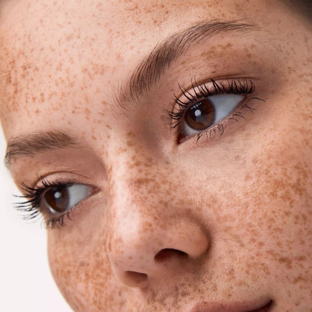 Nahaufnahme eines Gesichts mit Sommersprossen. Geschminkte Augen mit Mascara. Braune Augen.