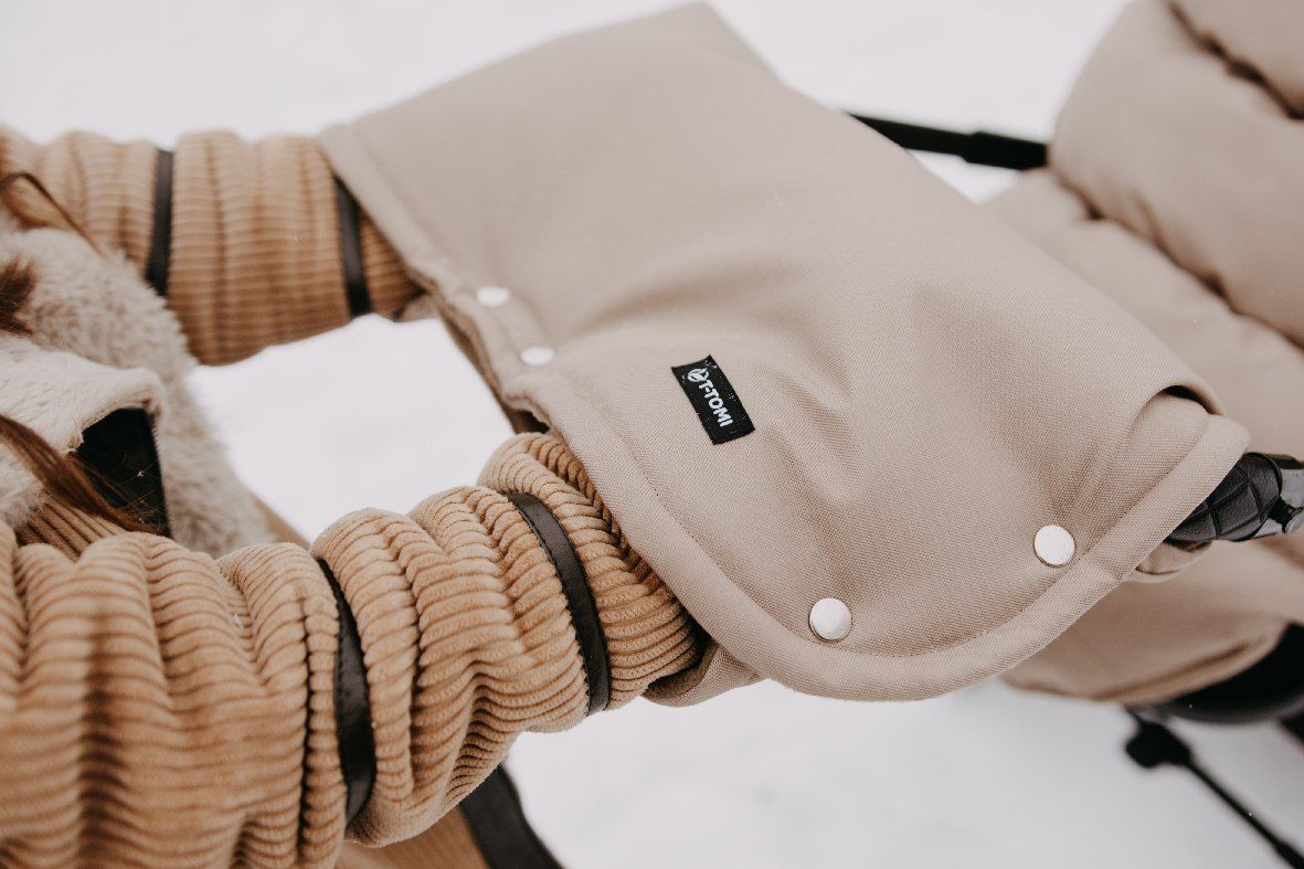 Beigefarbene Kinderwagen-Handwärmer aus Stoff mit Druckknöpfen und einem kleinen schwarzen Etikett.