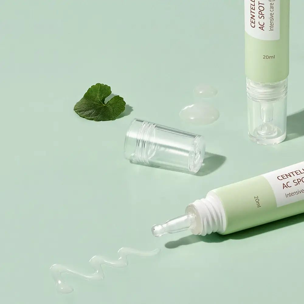 Zwei grüne Tuben mit Applikatoren. Aufschrift: Centella Calming AC Spot Cream. Ausgetretene Creme und Blätter.