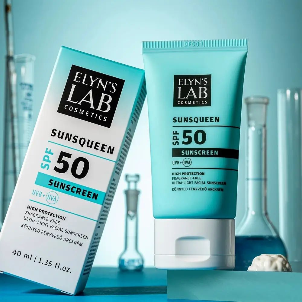 Türkisblaue Tube und Schachtel. Aufdruck: ELYN'S LAB, SUNSQUEEN SPF50, Sonnencreme. 40 ml. Hintergrund: Laborutensilien.