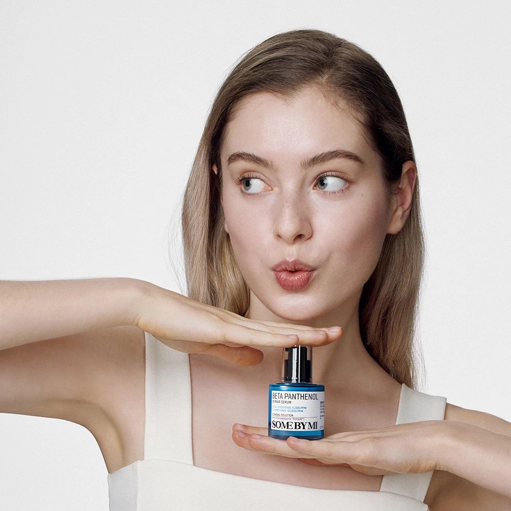 Junge Frau hält eine blaue Flasche vor sich. Auf der Flasche steht: Beta Panthenol Repair Serum, SOME BY MI. Hintergrund: weiß.