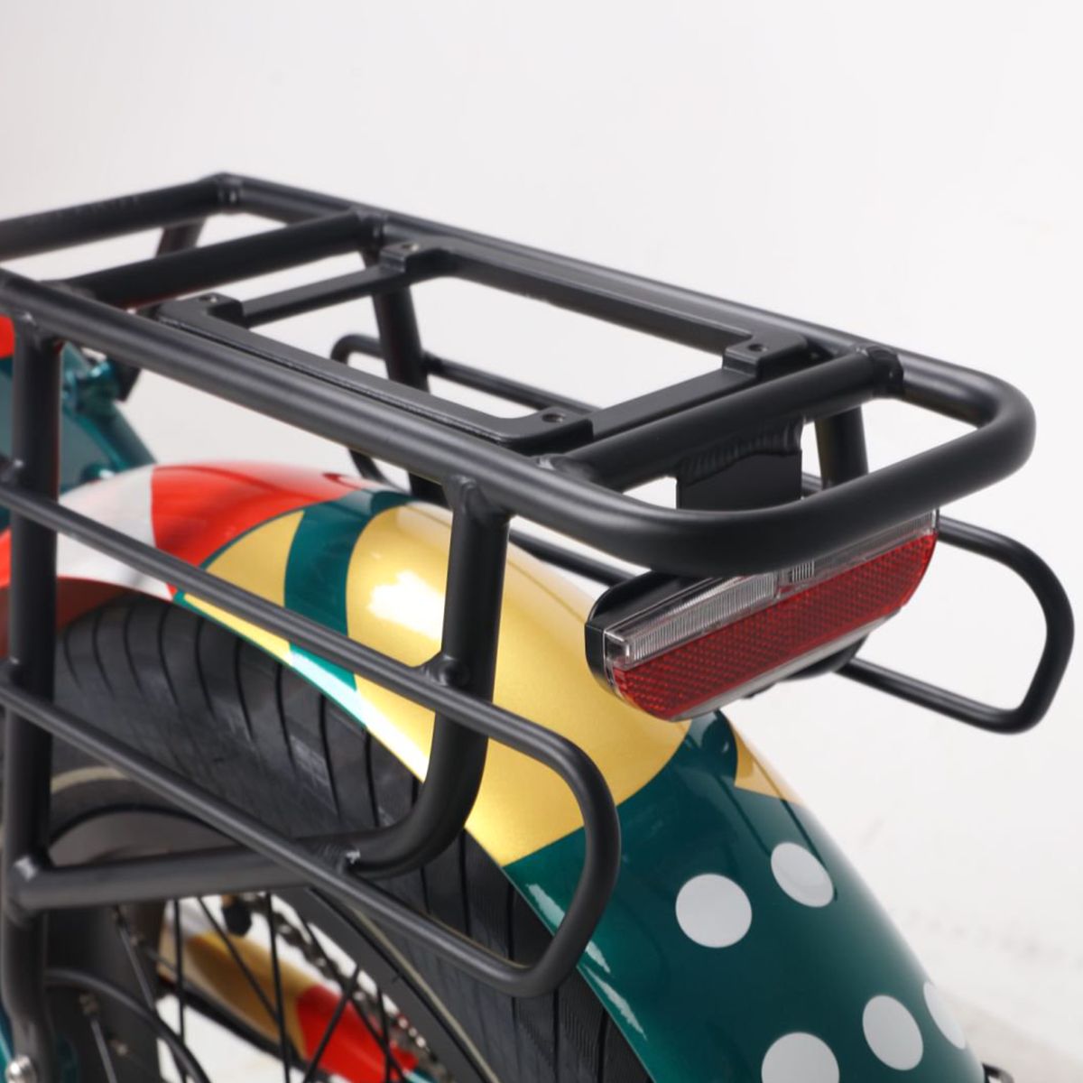 Gepäckträger und Rücklicht eines E-Bikes. Schwarzer Gepäckträger, rotes Rücklicht. Grün-gelbes Design des Schutzblechs mit weißen Punkten.
