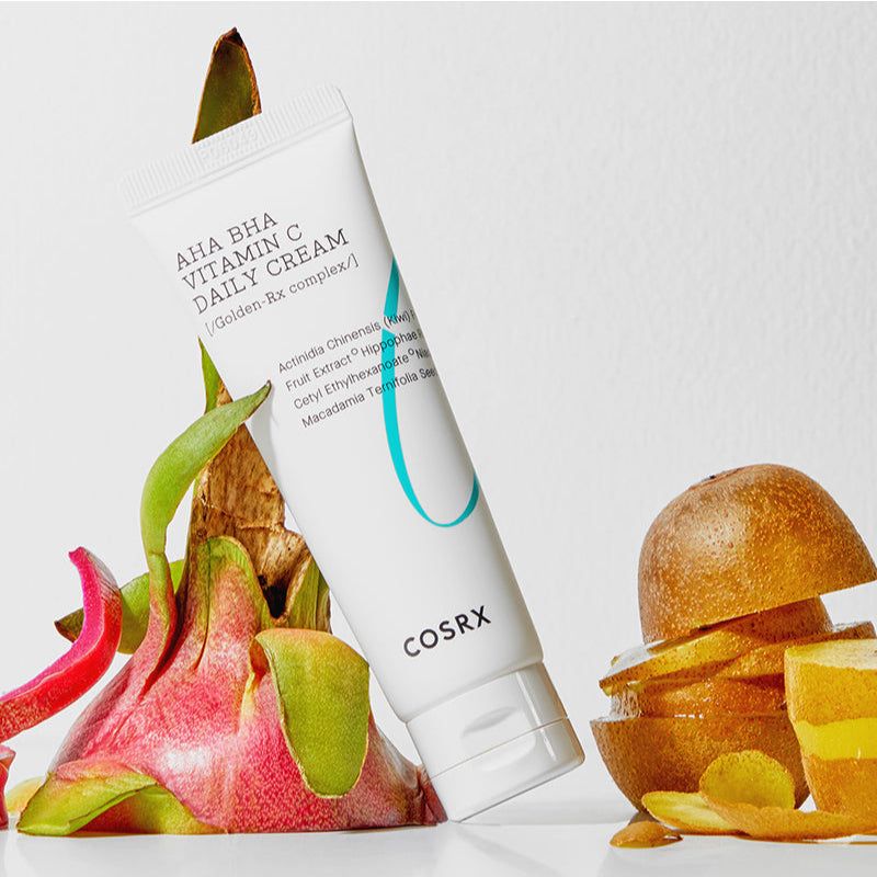 Weiße Tube mit AHA BHA Vitamin C Daily Cream, umgeben von Kiwi und Drachenfrucht. COSRX-Logo.