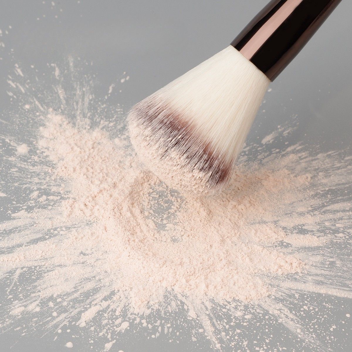 Ein Make-up-Pinsel mit weißen Borsten und einem dunklen Griff, der in hellrosa Puder getaucht ist.
