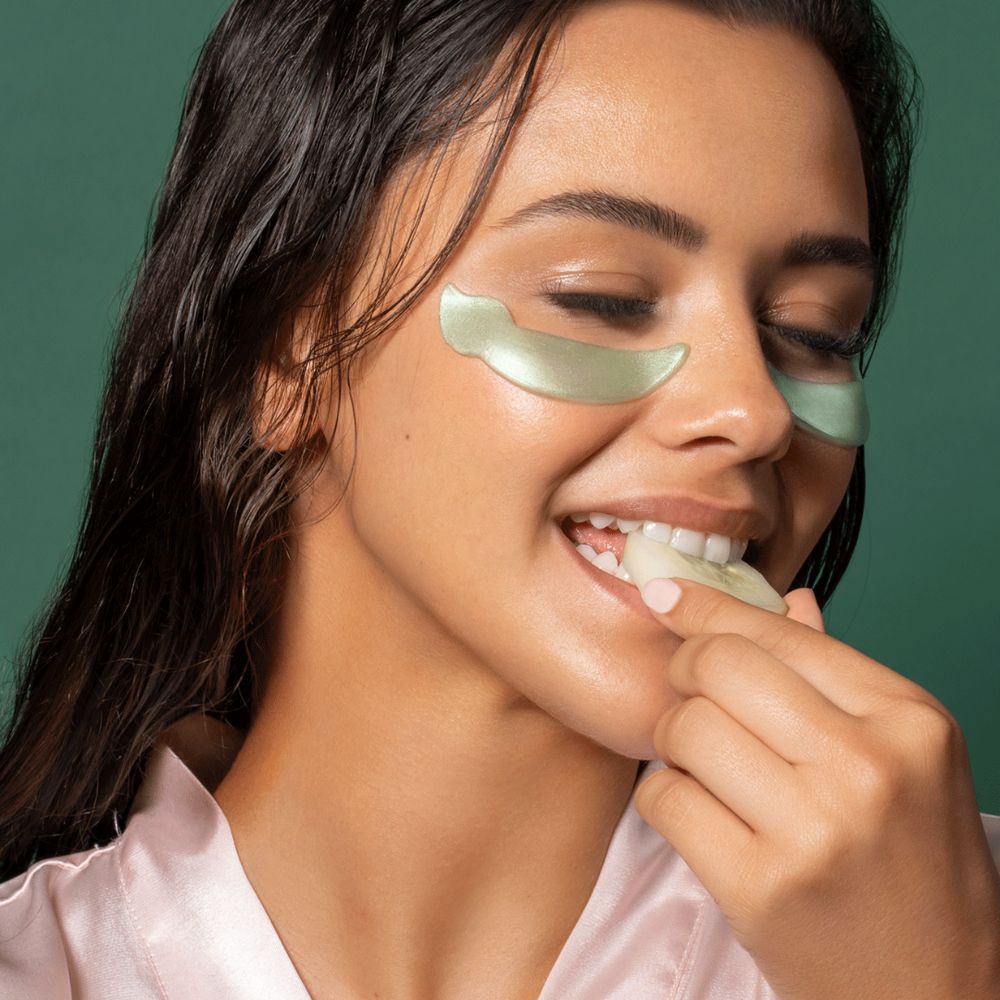 Frau mit Augenpads, die ein Stück Maske in den Mund nimmt. Grüne Augenpads.