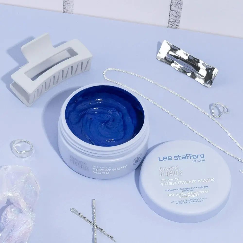 Geöffnete weiße Dose mit blauer Maske, daneben Haarschmuck und Schmuck auf hellem Untergrund.