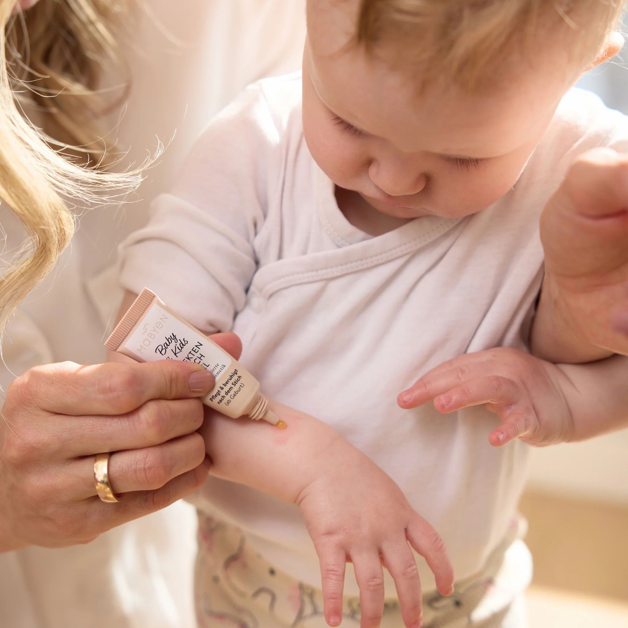 Eine Hand trägt MABYEN Insektenstich Gel auf den Arm eines Babys auf.