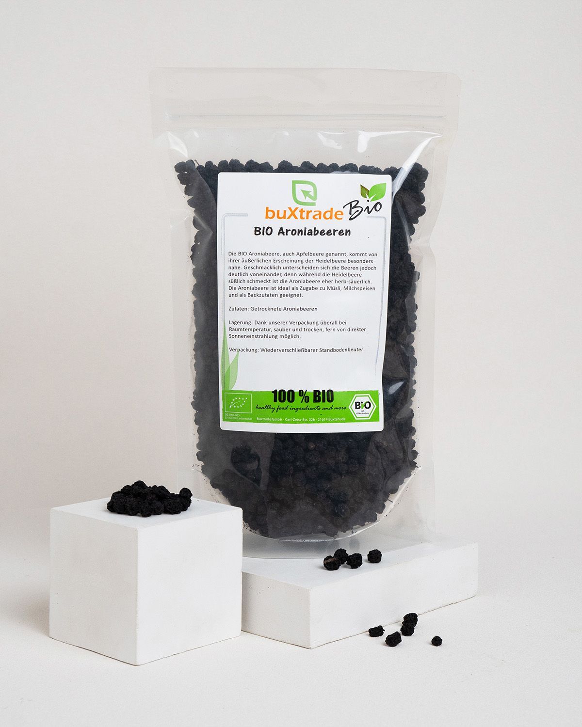 Transparente Tüte mit buXtrade Bio Aroniabeeren auf Podest. Bio-Siegel und Produktinformationen. Einige Beeren daneben.