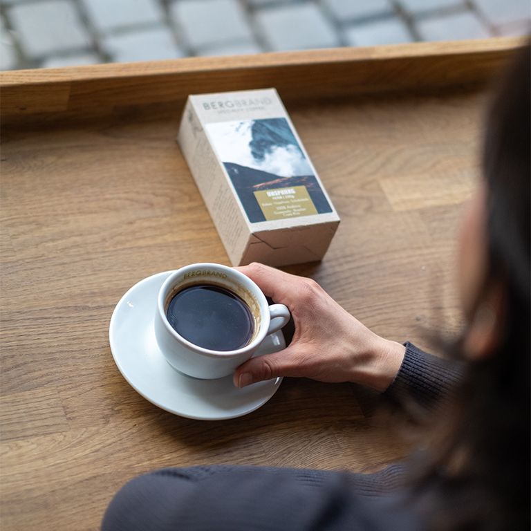 Kaffeetasse und Packung. Text: BERGBRAND. Kaffeetasse mit Kaffee. Packung mit Bergmotiv. Ursprung, Filter, 250g, 100% Arabica, Kakao, Haselnuss, Schokolade.