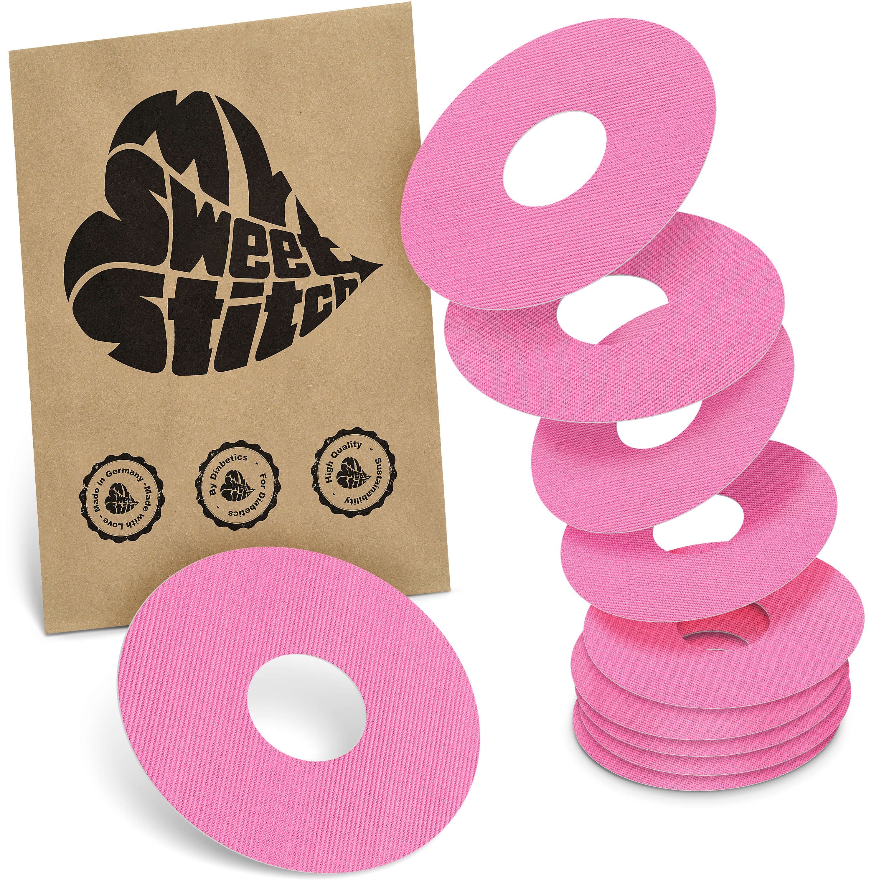 Fixierringe in Pink, neben brauner Verpackung mit Logo. Mehrere Ringe gestapelt und einzeln.