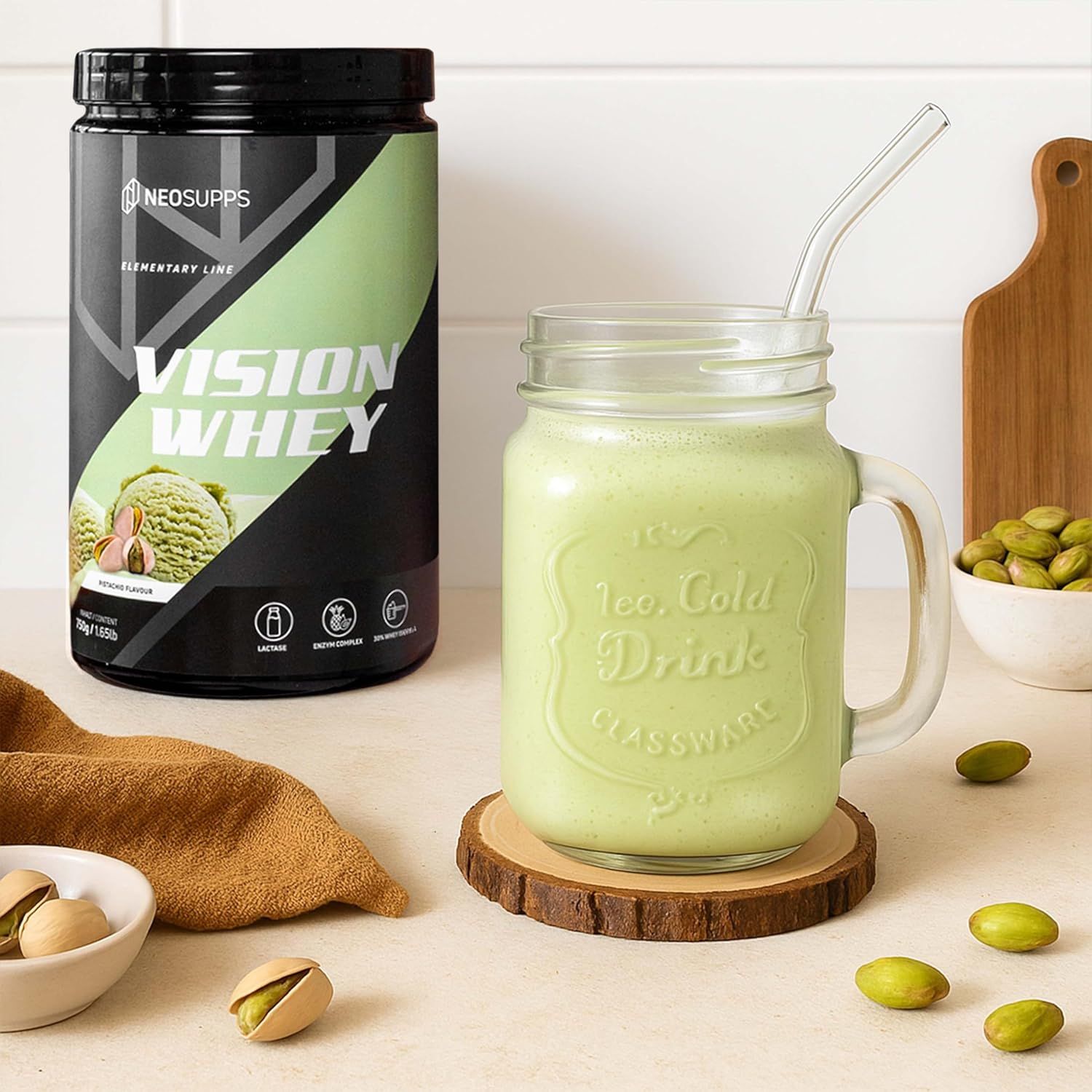 Dose Vision Whey Pistachio neben Glas mit grünem Getränk und Strohhalm. Pistazien und Holzbrettchen. Aufschrift: Vision Whey.