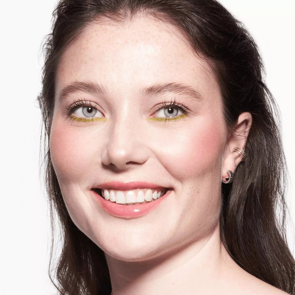 Porträt einer Frau mit Kajal auf den Augenlidern. Sie lächelt. Rosa Wangen, helle Haut.