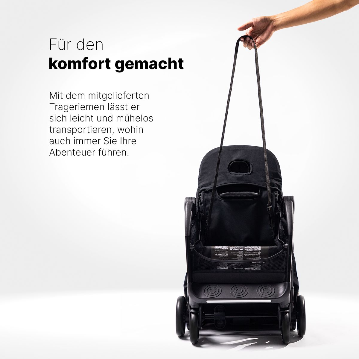 Schwarzer, gefalteter Kinderwagen, an Trageriemen gehalten. Text: Für den Komfort gemacht.