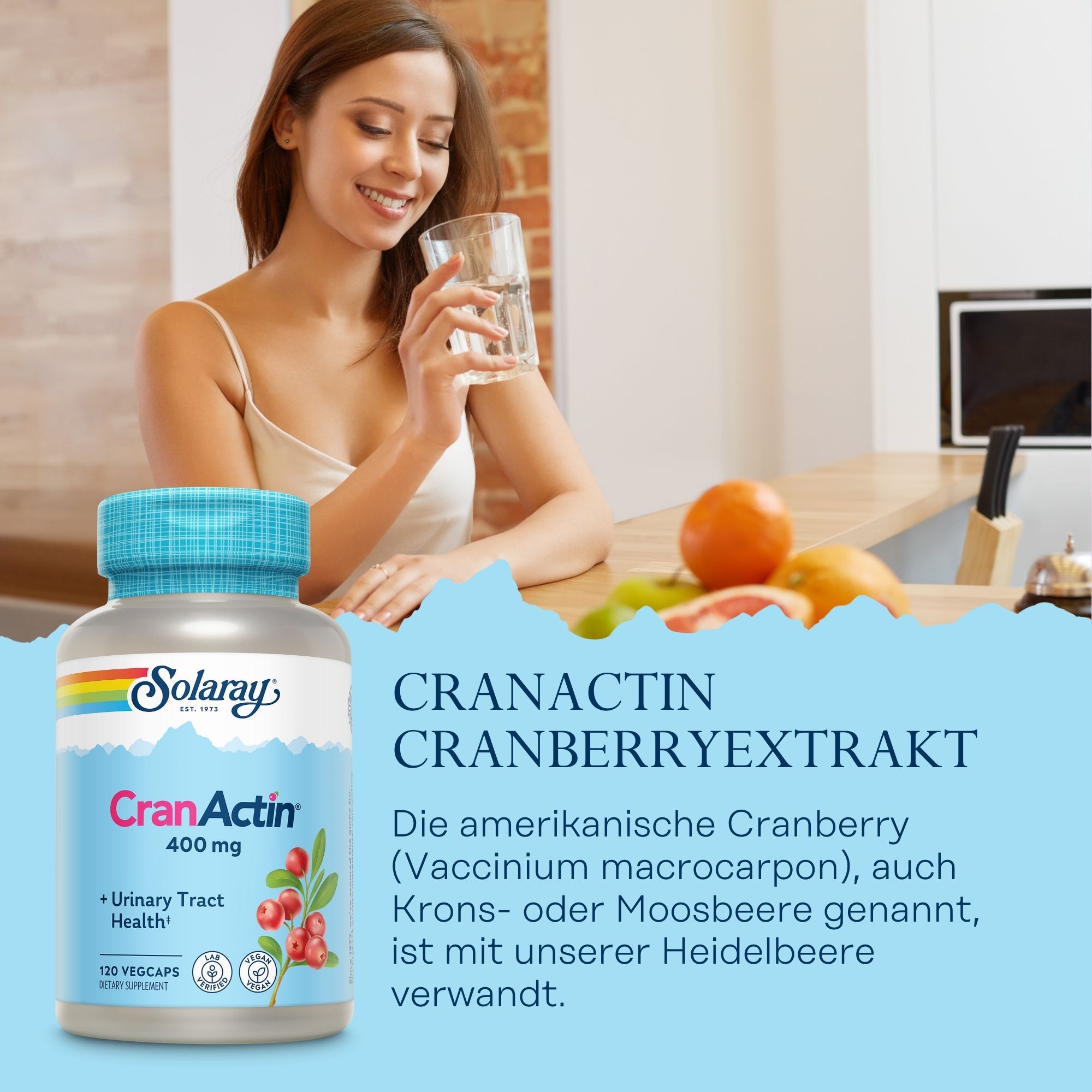 Eine Flasche mit CranActin 400 mg. Aufschrift: Urinary Tract Health. 120 Vegcaps. Frau trinkt Wasser. Obst auf der Theke.