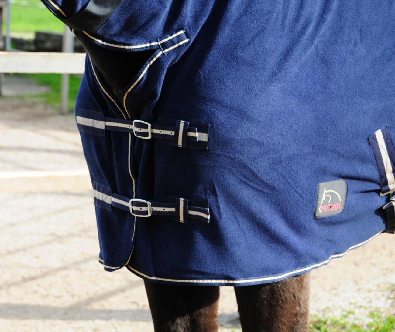 Detail der blauen AMKA Abschwitzdecke mit Halsteil. Silberne Schnallen und Kreuzgurte sind sichtbar. Logo auf der Seite.