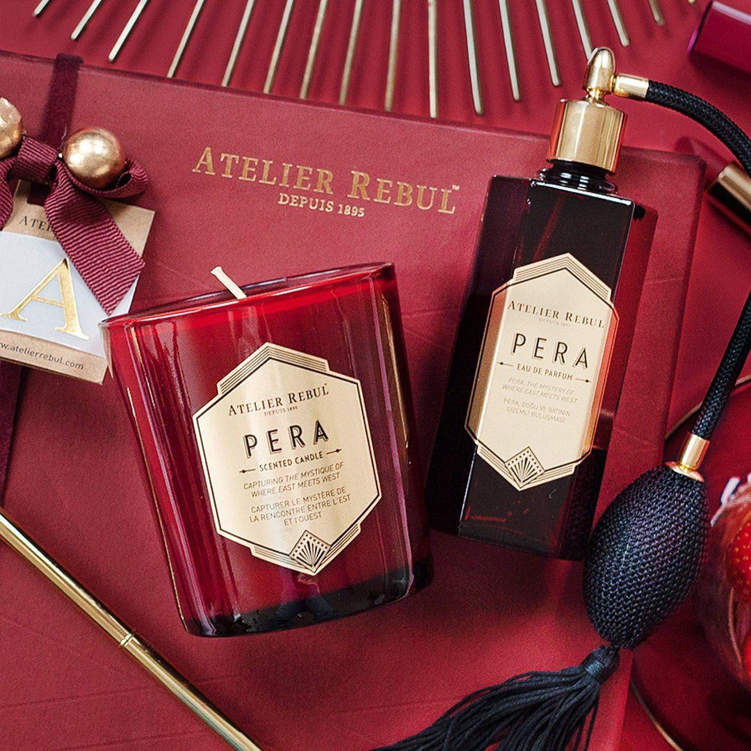 Rote Kerze und Flakon mit goldener Kappe. Beide mit Etikett "Pera" von Atelier Rebul. Auf rotem Hintergrund.
