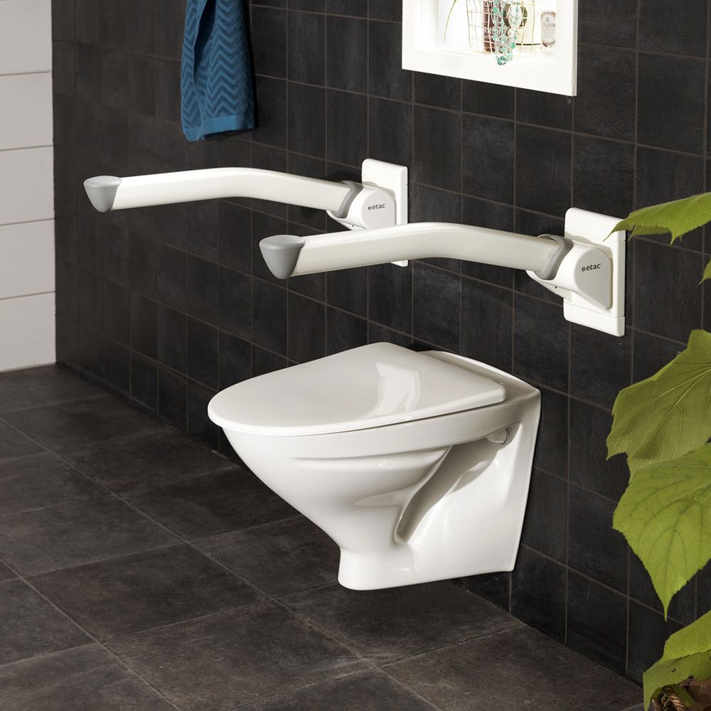 Zwei weiße Stützklappgriffe über einer Toilette an einer dunklen gefliesten Wand.