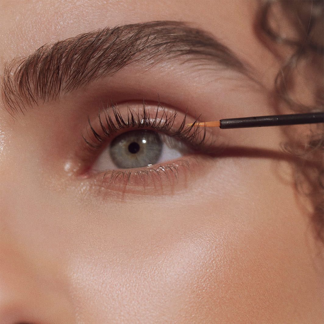 Nahaufnahme eines Auges. Wimpern werden mit einem Applikator behandelt. Hautton. Helle Augenfarbe.