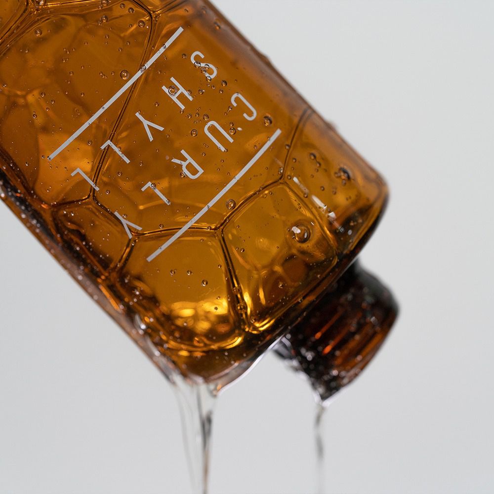Braune Shampoo-Flasche, aus der Flüssigkeit fließt. Text: CURLY SHYLL.