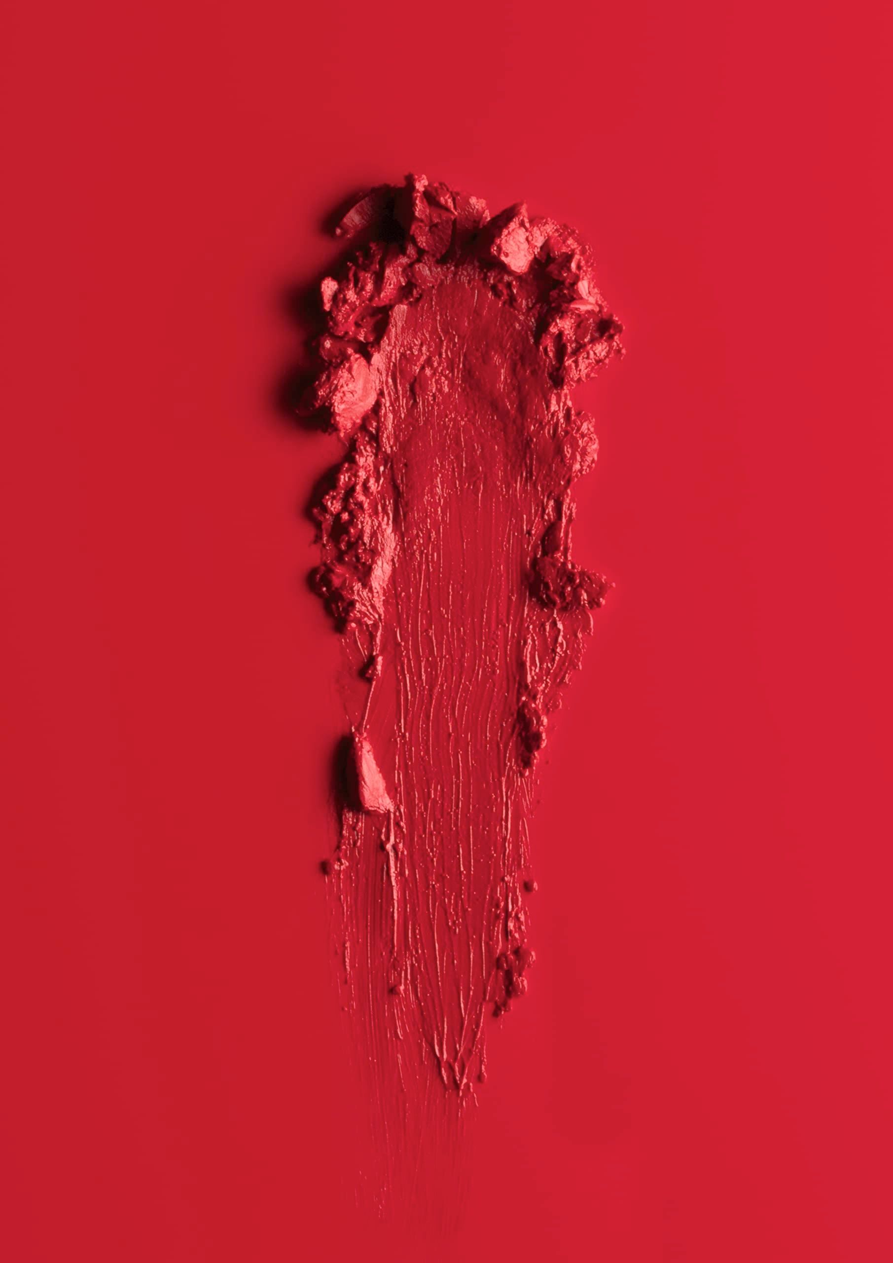 Abstrich von rotem Lippenstift auf rotem Hintergrund. Textur mit sichtbaren Partikeln und Pinselstrichen.