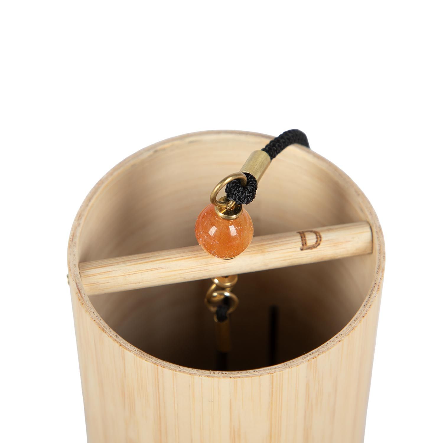 Nahaufnahme des Klangspiels. Bambus, orangefarbener Stein, Holzstab mit 'D'. Schwarze Schnur. Goldfarbene Details.