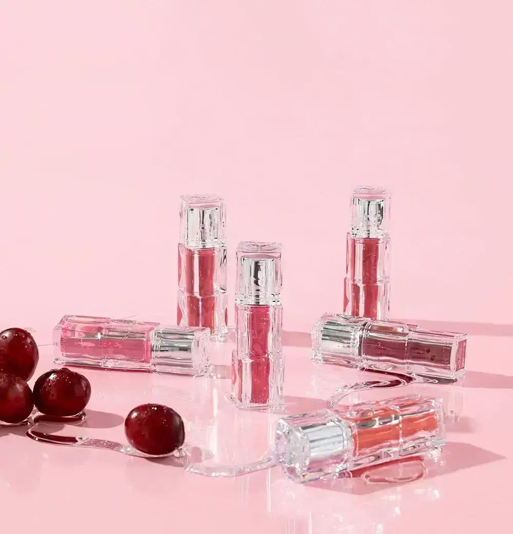 Mehrere Lippen-Tints in transparenten Behältern mit silbernen Deckeln, umgeben von Kirschen.