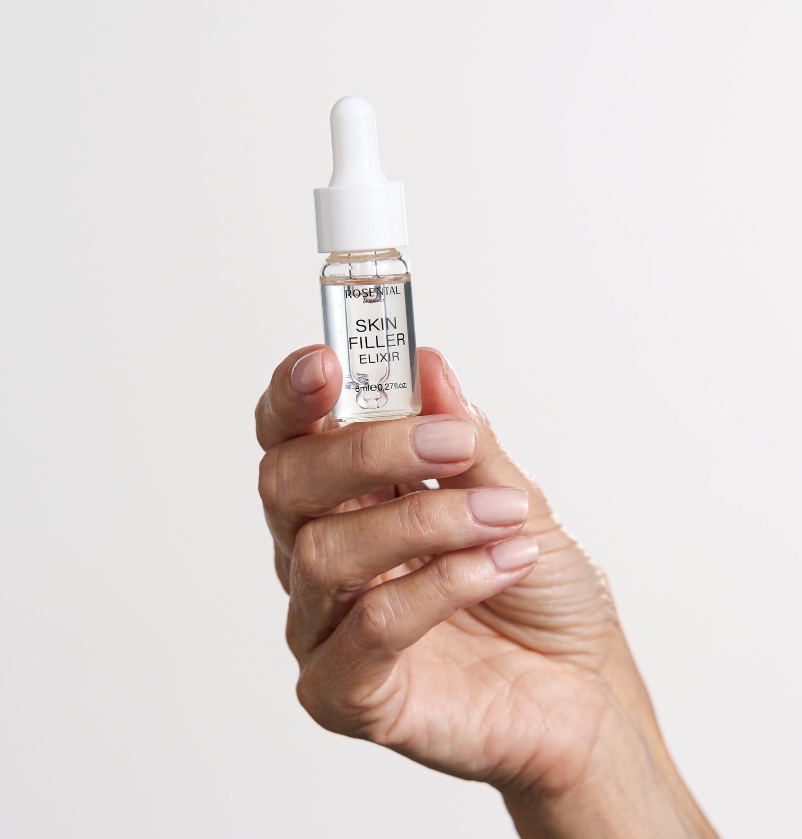 Hand hält ein Fläschchen Skin Filler Elixir. Das Fläschchen ist transparent und hat einen weißen Deckel.