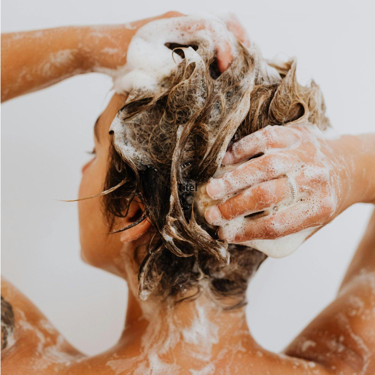 Person wäscht Haare mit Schaum. Hände massieren Kopfhaut. Rückansicht.