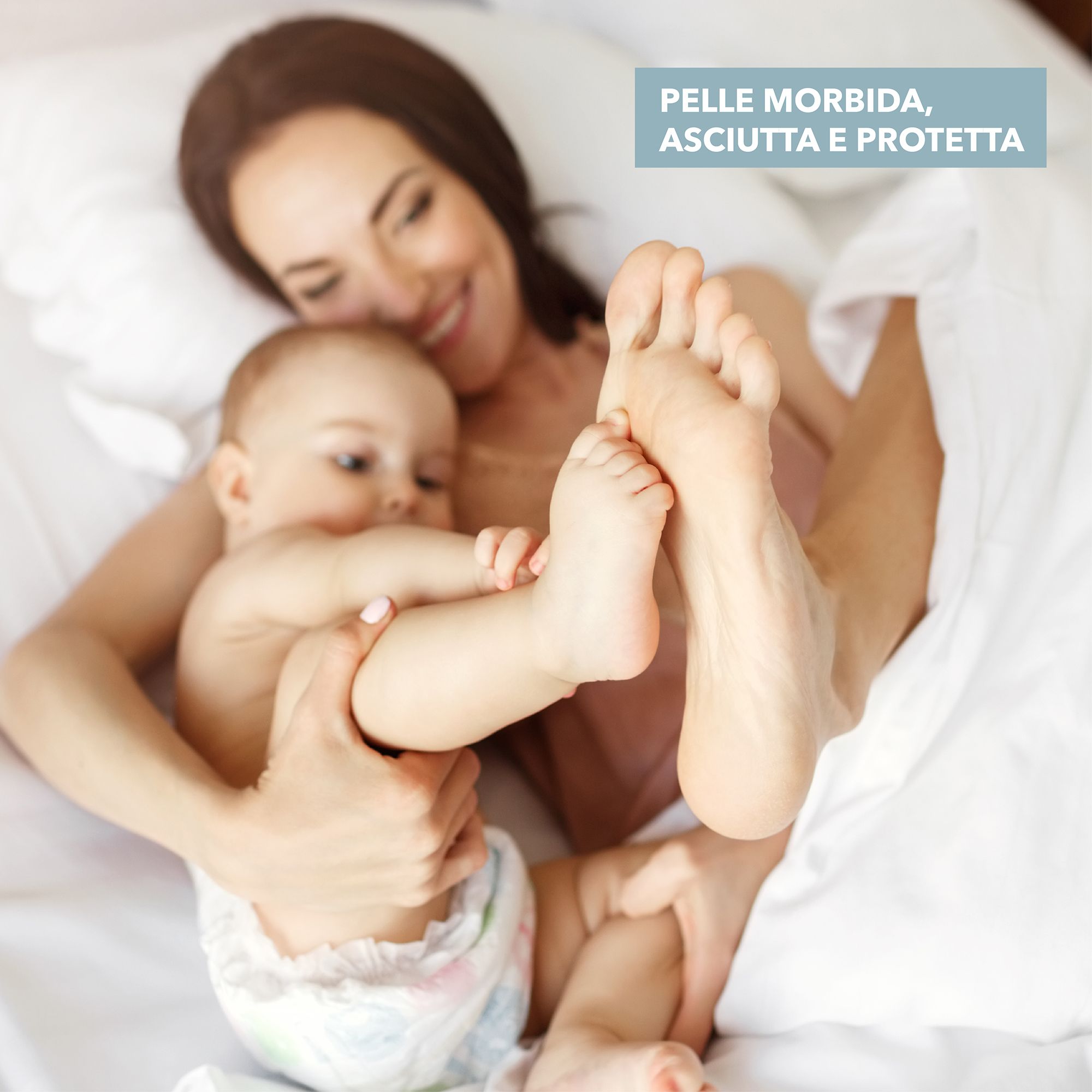 Mutter und Baby im Bett. Babyfüße im Fokus. Text: Weiche, trockene und geschützte Haut. Baby trägt Windel.