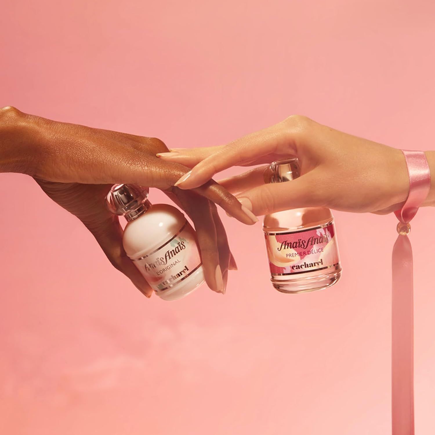 Zwei Hände halten Cacharel Anais Anais Flakons. Einmal L'Original, einmal Premier Delice. Rosa Hintergrund.