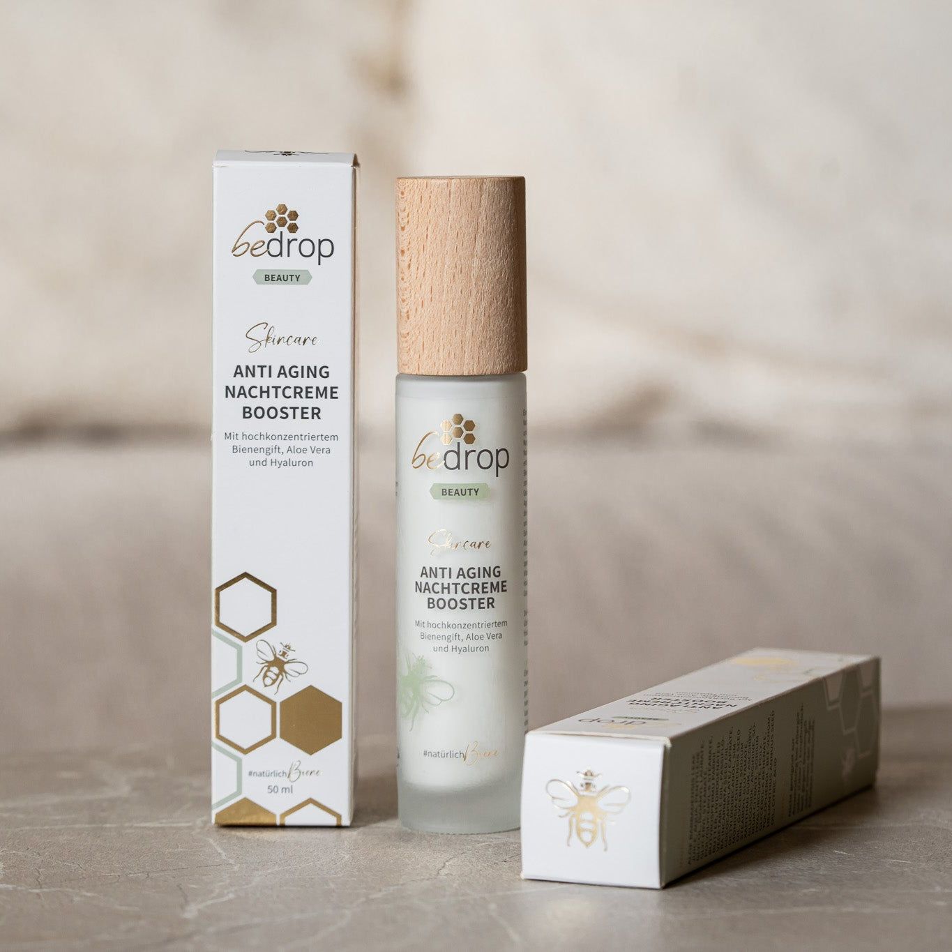 Eine Flasche und zwei Verpackungen der Anti-Aging Nachtcreme Booster. Aufschrift: bedrop Beauty, Anti Aging Nachtcreme Booster.