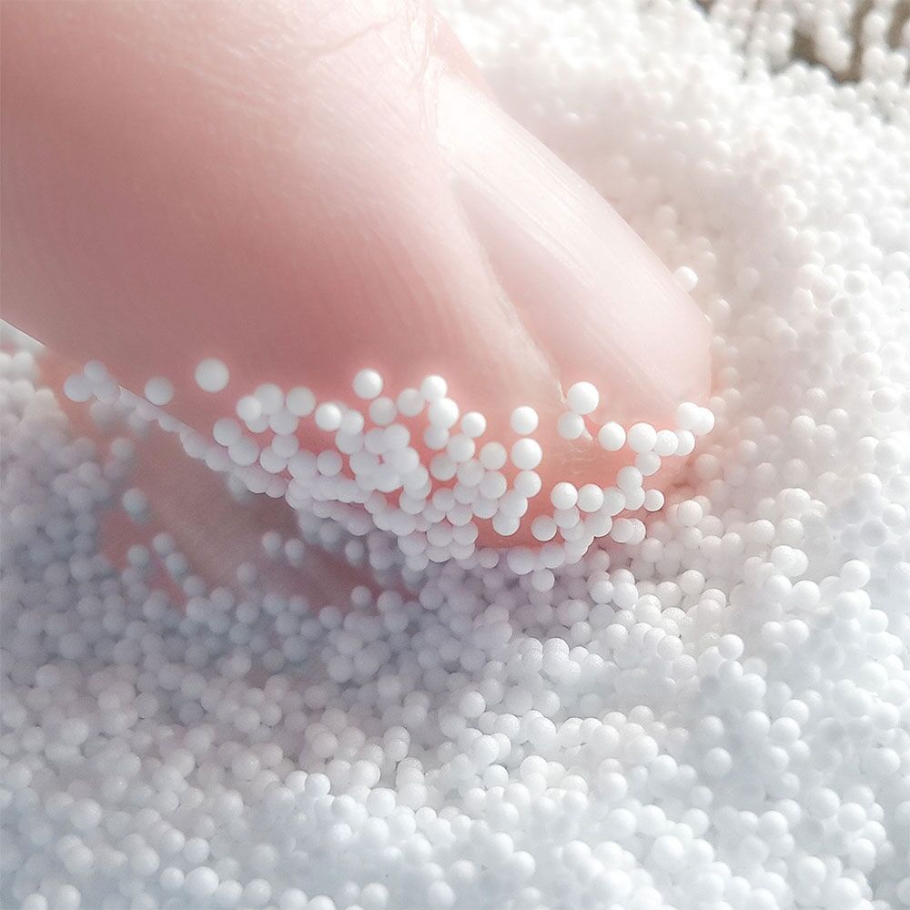 Nahaufnahme einer Hand, die in weiße Kügelchen drückt. Kleine, runde Partikel.