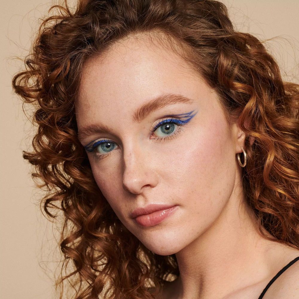 Nahaufnahme einer Frau mit Make-up. Blauer Eyeliner, Lidschatten, Lippenstift. Hautton, rote Locken.