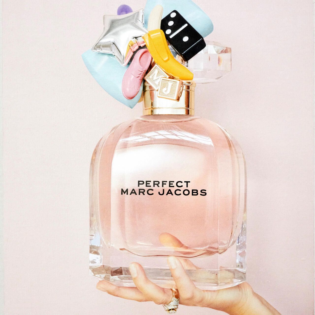 Parfümflakon mit dekorativem Deckel. Aufschrift: PERFECT MARC JACOBS. Flakon wird von einer Hand gehalten. Ring am Finger.