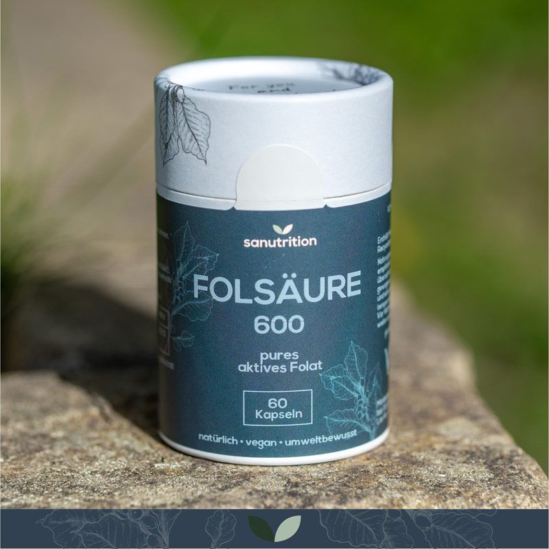 Zylindrische Dose "Sanutrition Folsäure 600" auf Stein. Enthält 60 Kapseln. Hintergrund: unscharfes Grün.