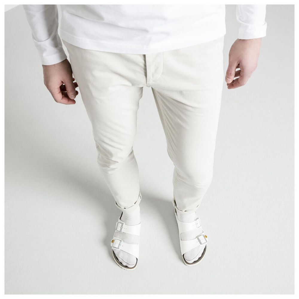 Person trägt weiße Sandalen mit zwei Riemen. Beige Hose und weißes Oberteil. Draufsicht.