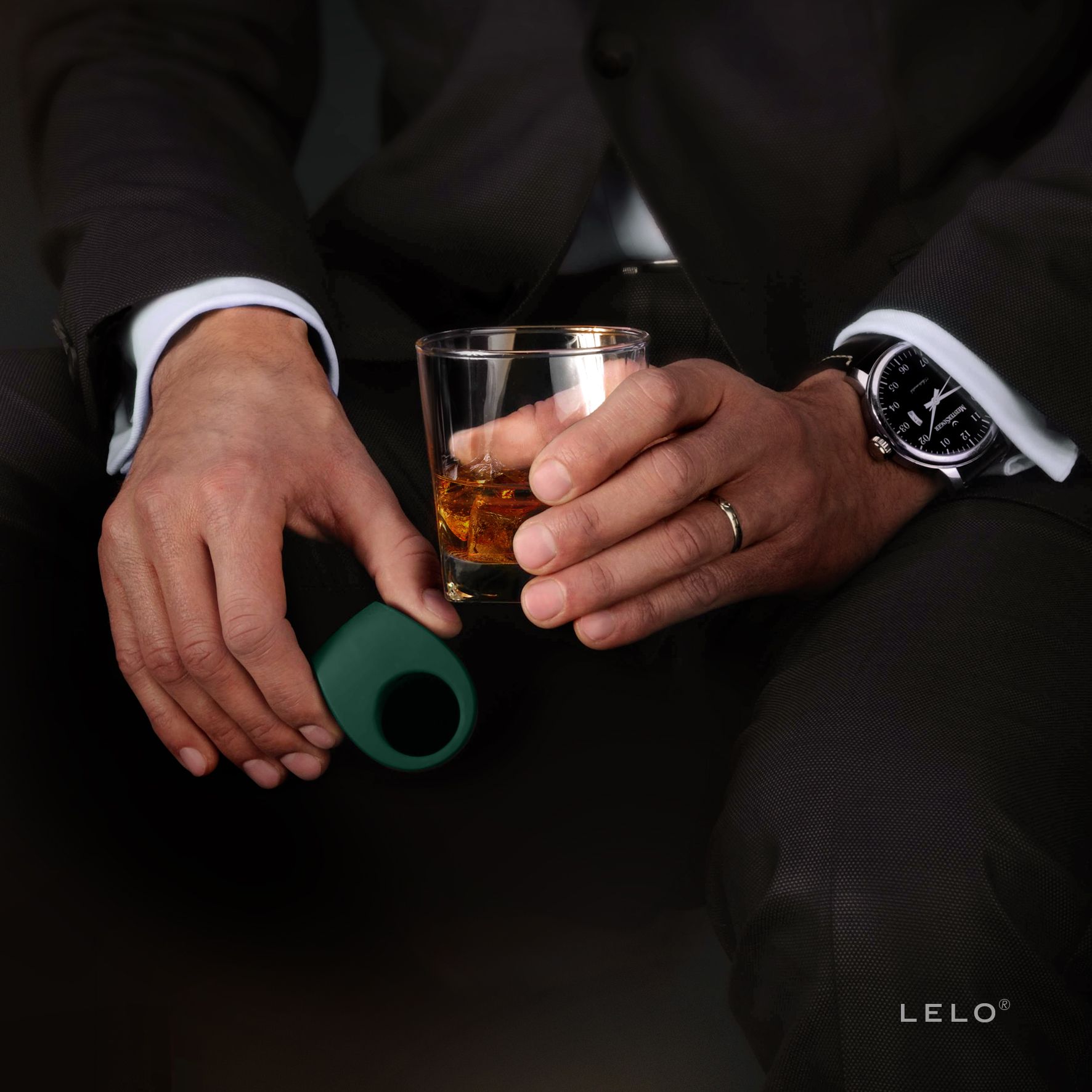 Mann hält dunkelgrünen Vibrationsring und ein Glas Whisky.