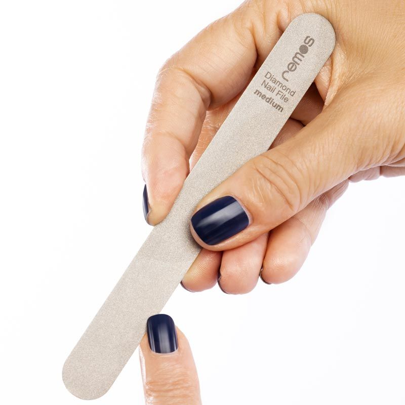 Hand hält eine graue Feile. Aufschrift: remos Diamond Nail File medium. Ein Nagel wird gefeilt.