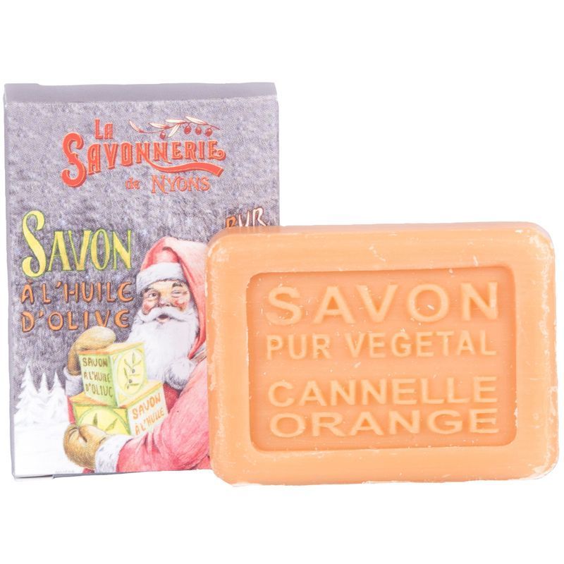 Orangener Seifenblock mit Schriftzug SAVON PUR VEGETAL CANNELLE ORANGE. Daneben eine Verpackung mit Weihnachtsmann-Illustration.