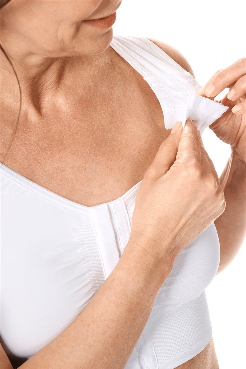 Weiße BH-Träger werden von einer Frau geöffnet. Der BH hat einen Frontverschluss.